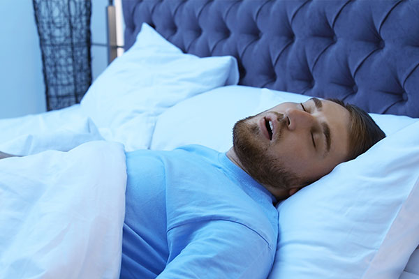 A man lying down on a bed with his eyes closed.