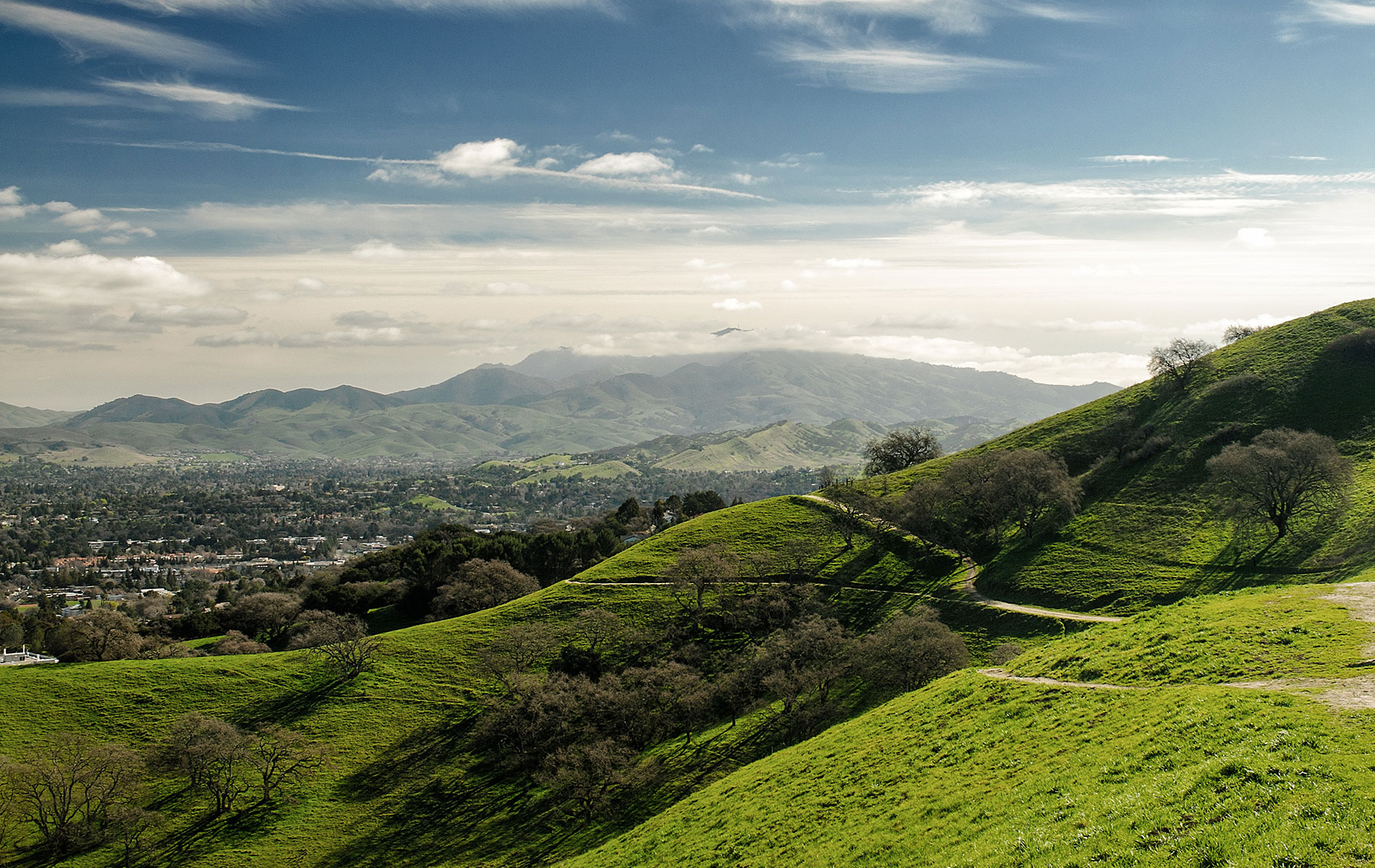 The image shows a picturesque landscape featuring rolling green hills, a winding road leading upwards, and a clear blue sky.